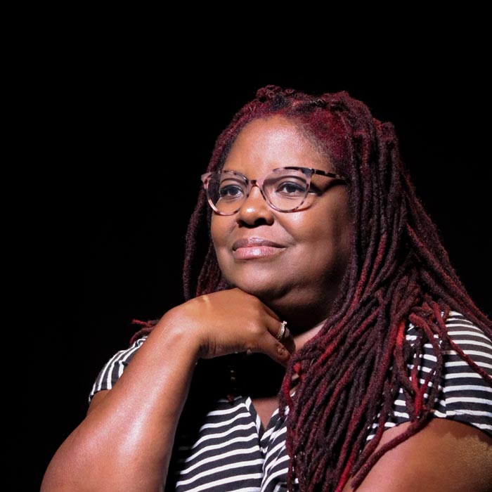 A smiling woman sits in front of a black background.