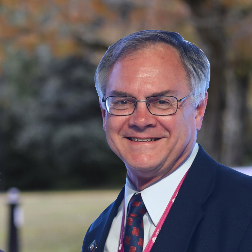 A smiling man in a suit stands outside.
